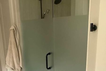 Frameless glass shower door with white tile and black hardware