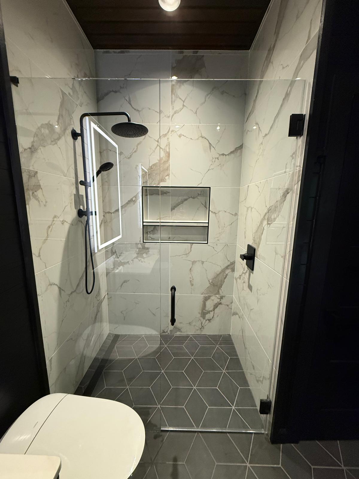 Frameless glass shower door against a white marble wall