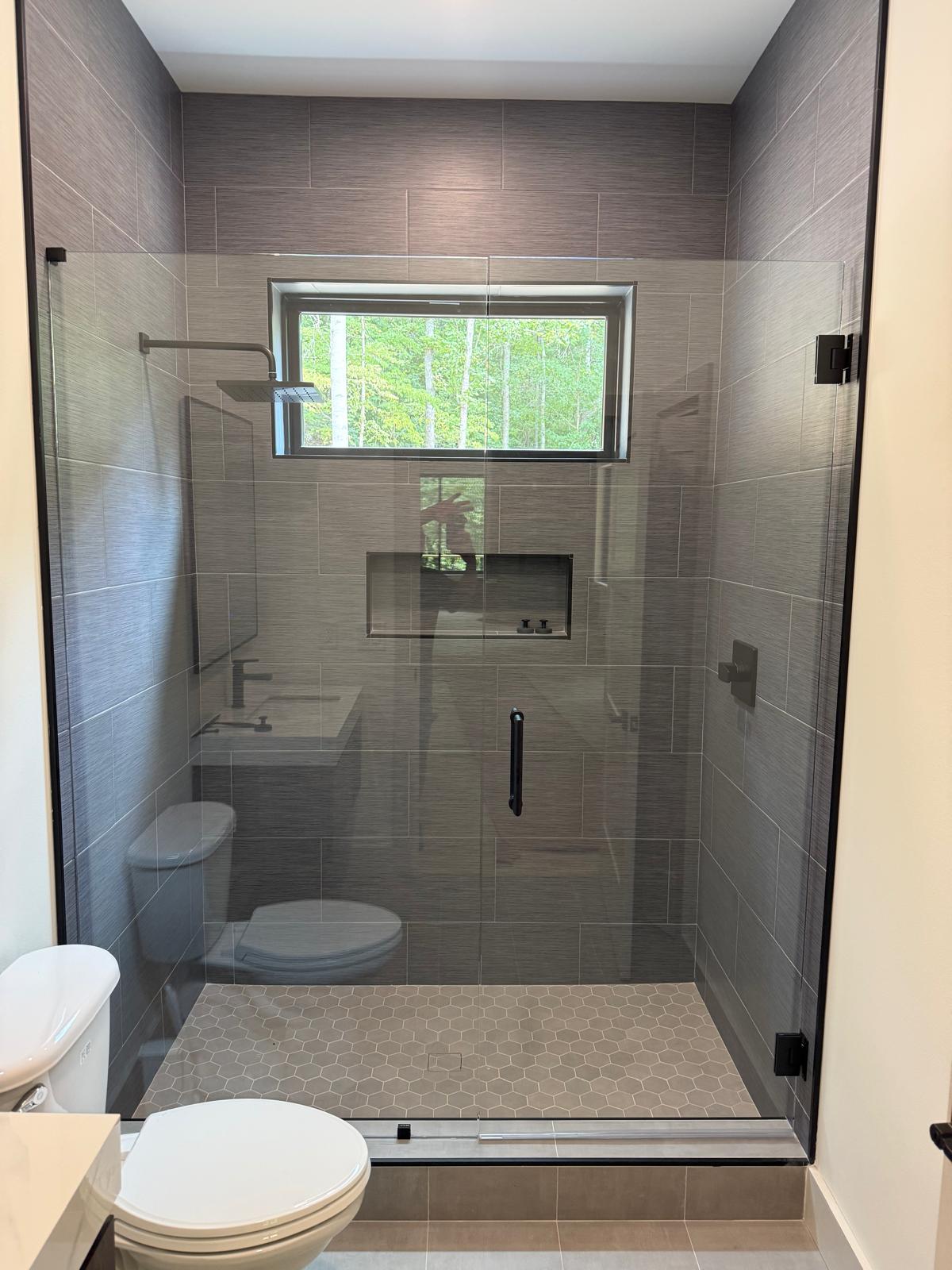 Glass shower door with gray tile and a window