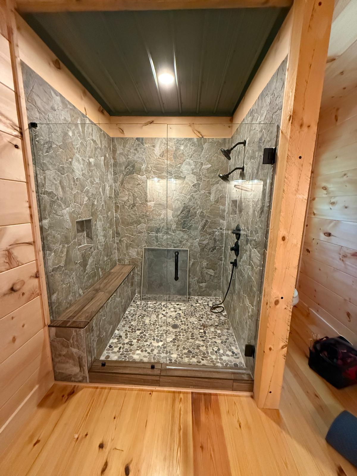 Frameless glass shower in a rustic bathroom with stone tile and wood walls