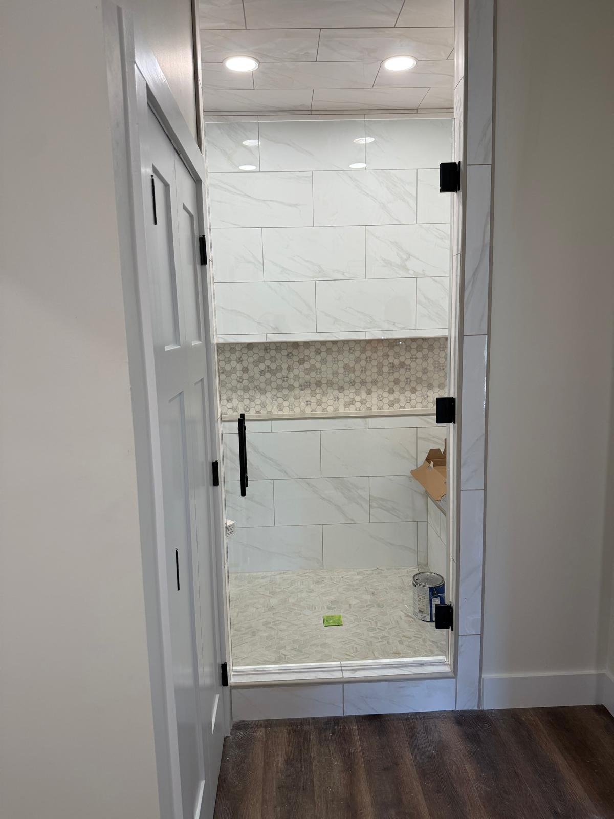 Glass shower door with white tile and a tiled niche
